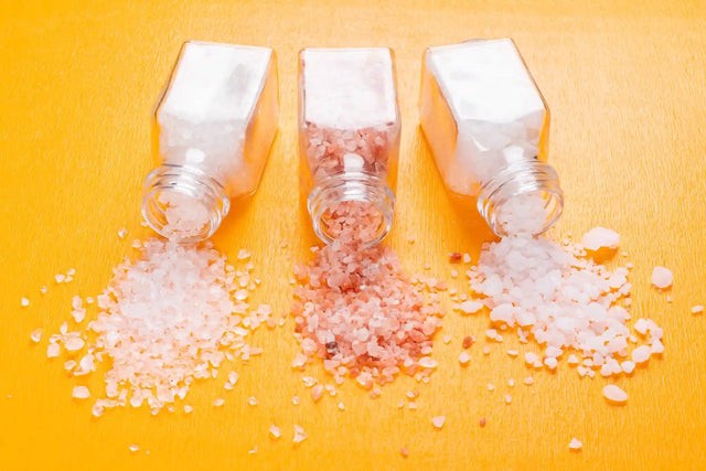 Spilled Himalayan and sea salt from glass jars, representing salt sensitivity and its impact on health