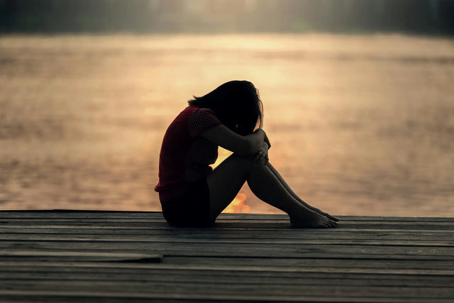 Woman suffering from fibromyalgia sitting in pain beside a lake.