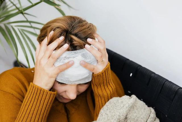 Woman with head bandage holding head in pain, emphasizing the need to learn how to prevent menstrual migraines